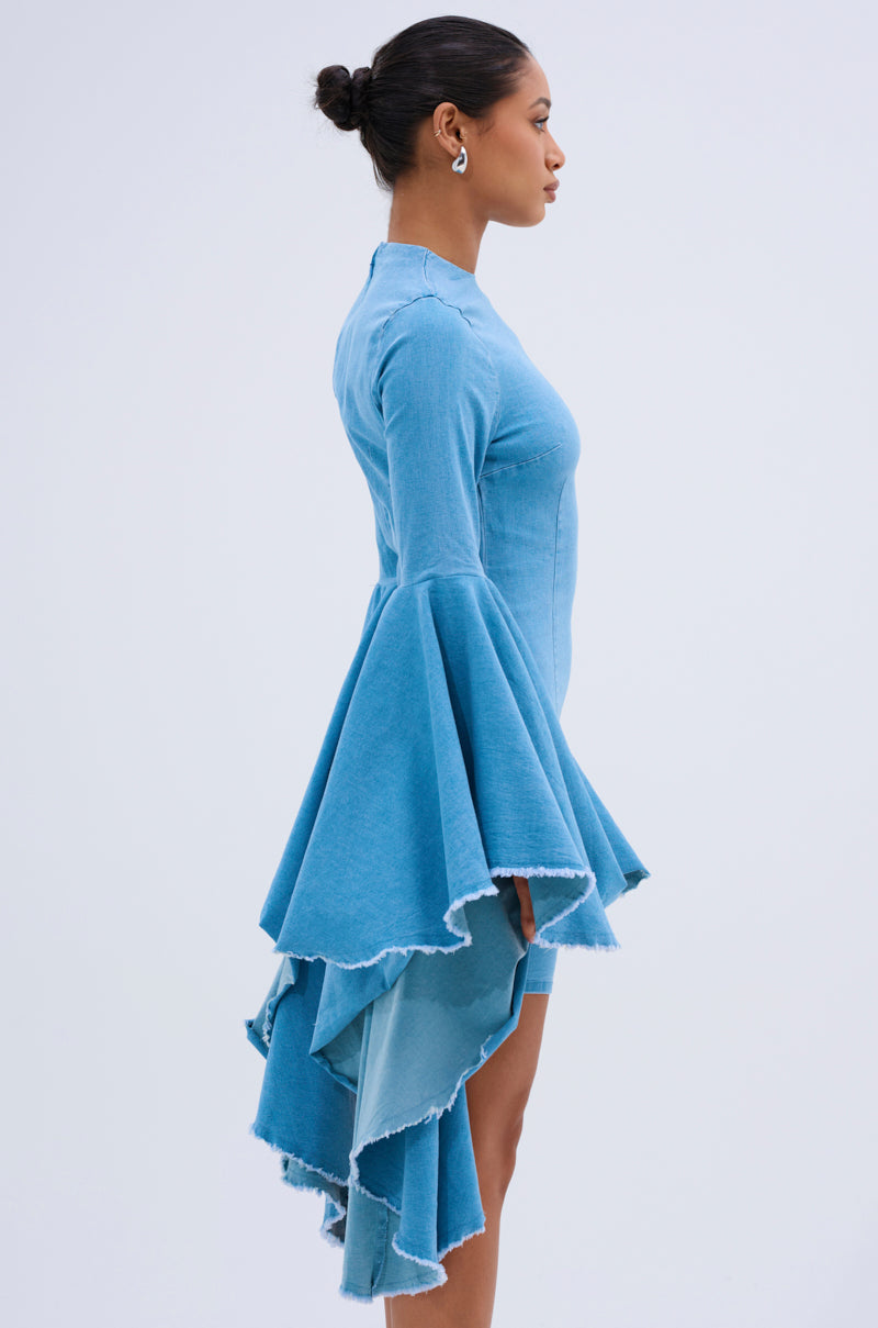 A woman in profile models the SHE'S ROYAL DENIM LONG SLEEVE MINI DRESS featuring tiered, ruffled high-low sleeves and fringe hems. Her hair is in a neat bun, and she wears hoop earrings against a plain light background.