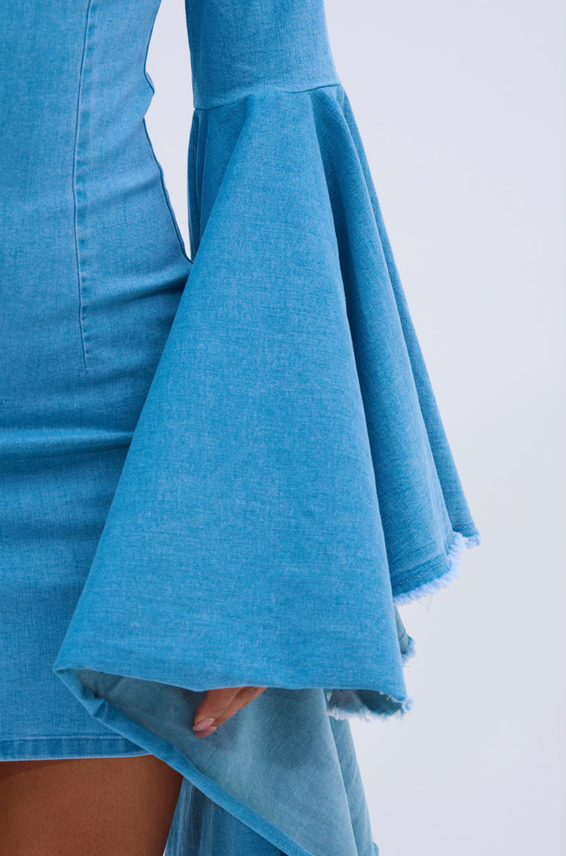 A close-up of someone wearing the SHE'S ROYAL DENIM LONG SLEEVE MINI DRESS, featuring dramatic bell sleeves, frayed hem, and bodycon fit; the person's hand is visible near the wide, flowing sleeve.
