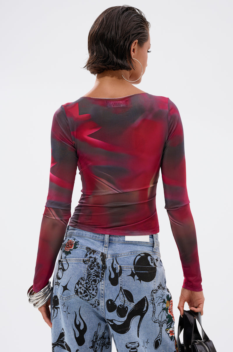 A person with short dark hair stands with their back to the camera, wearing the AURA LONG SLEEVE MESH TOP in red and light blue jeans with bold black abstract patterns, and holding a black handbag.
