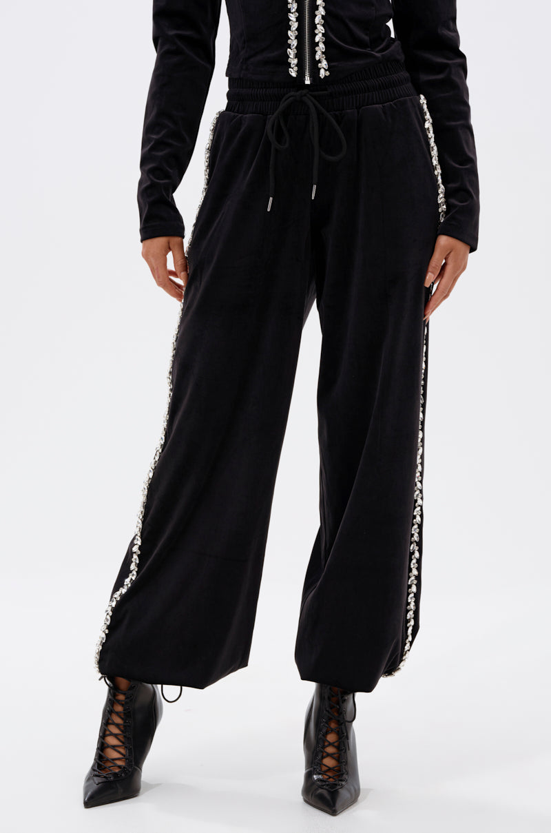 A person wearing the DARA RHINESTONE WIDE LEG SWEATPANT, featuring decorative trim on the side seams, paired with a black top and black lace-up ankle boots. The photo is cropped from the shoulders down.