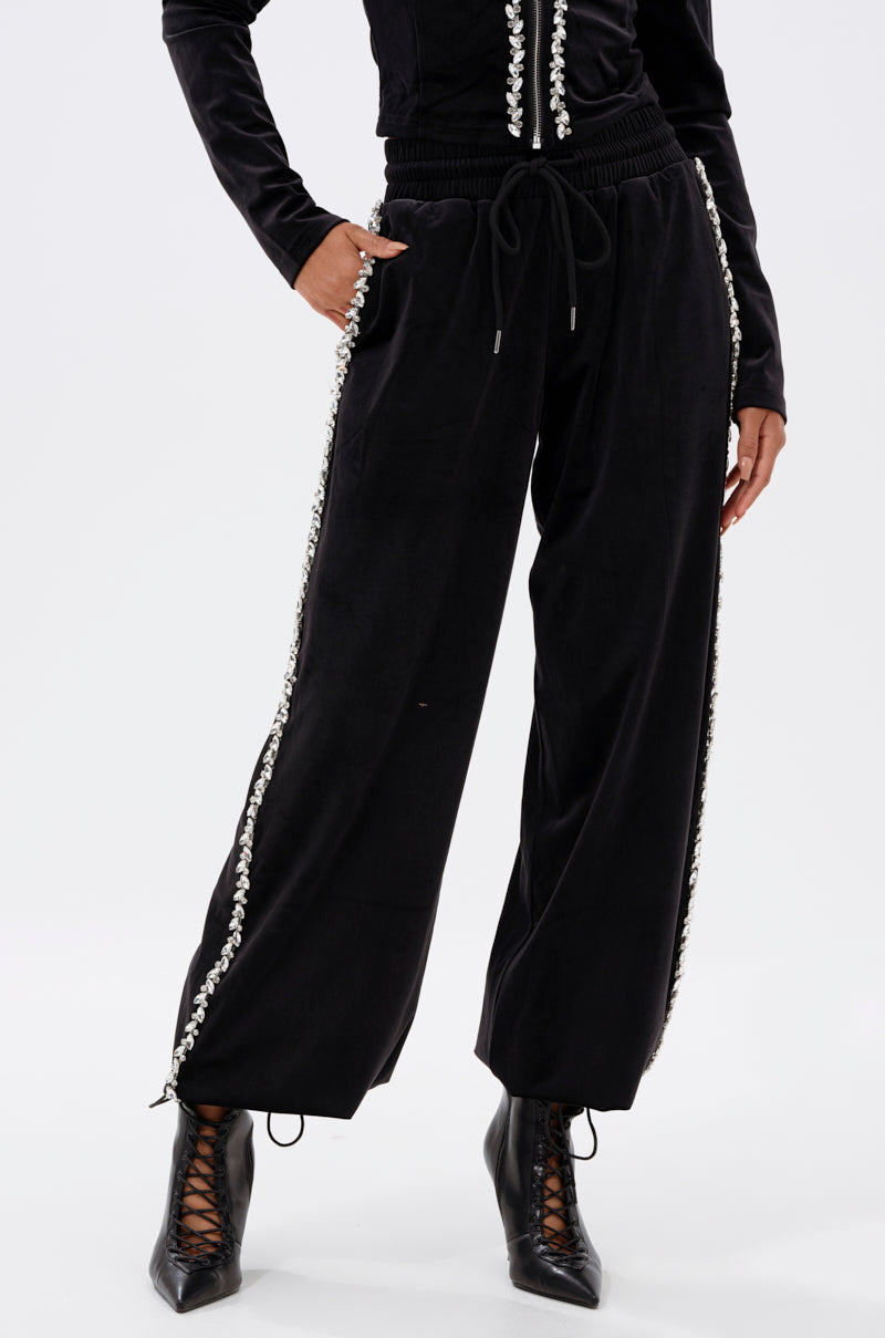 A person wears DARA RHINESTONE WIDE LEG SWEATPANT, black with decorative side trim, and black lace-up ankle boots, shown from the waist down against a plain white background.