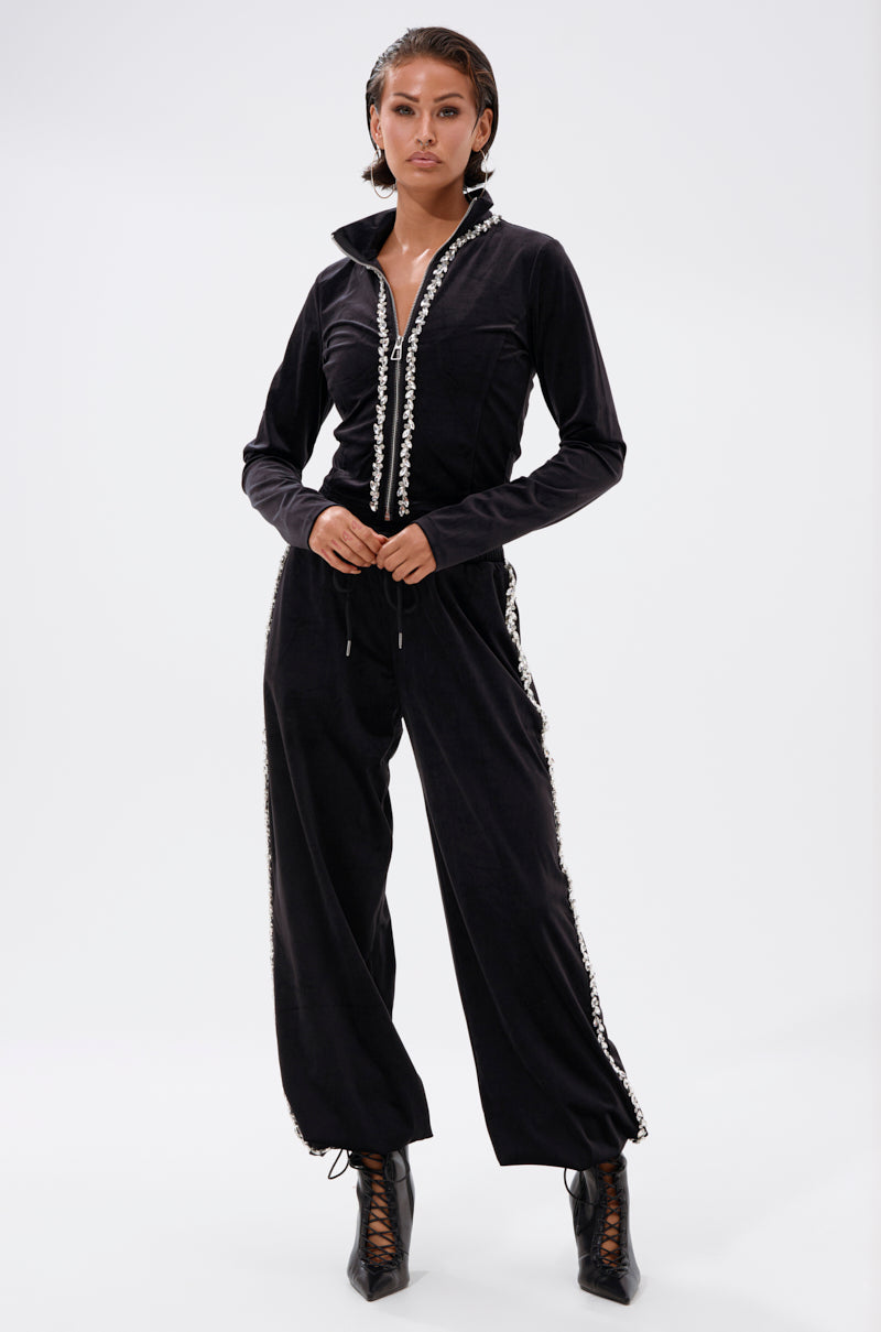 A woman stands confidently in the DARA RHINESTONE WIDE LEG SWEATPANT, styled with black lace-up ankle boots and slicked-back hair, against a plain white background.