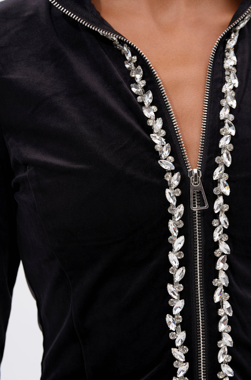 Close-up of the DARA RHINESTONE MOCK NECK ZIP-UP SWEATSHIRT: a black zip-up with a silver zipper bordered by clear, leaf-shaped rhinestones. The top of the chest and neck is visible, showcasing its decorative, elegant style.
