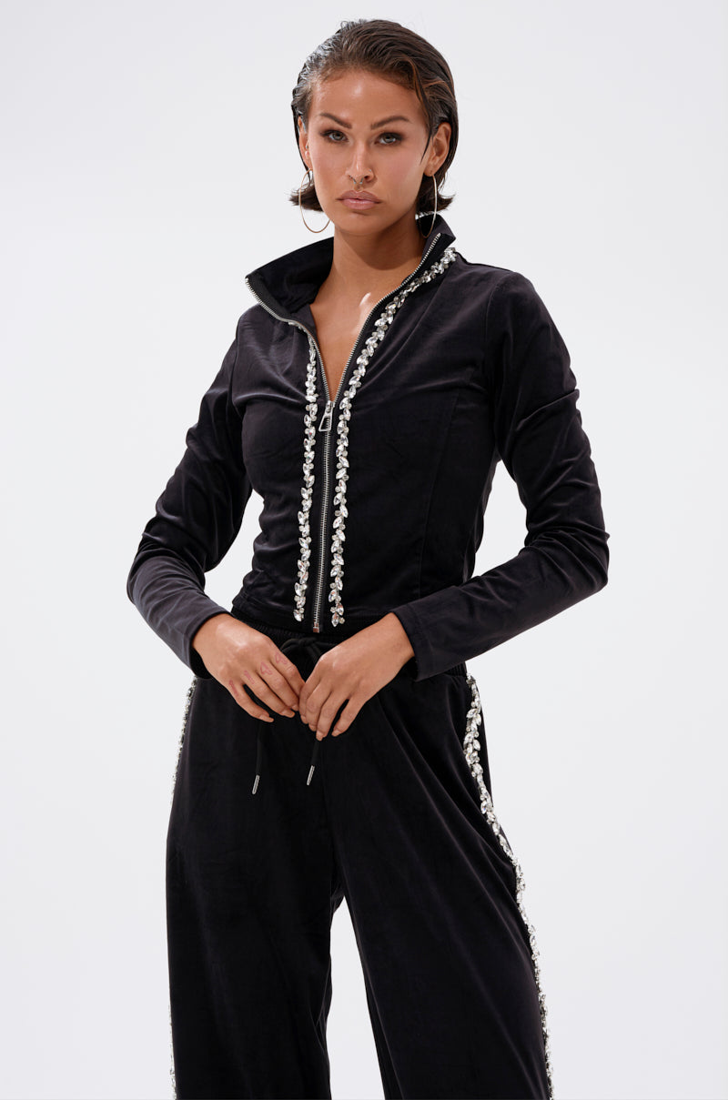 A woman wears the DARA RHINESTONE MOCK NECK ZIP-UP SWEATSHIRT with matching velour pants featuring pearl-like embellishments, standing against a plain white background.