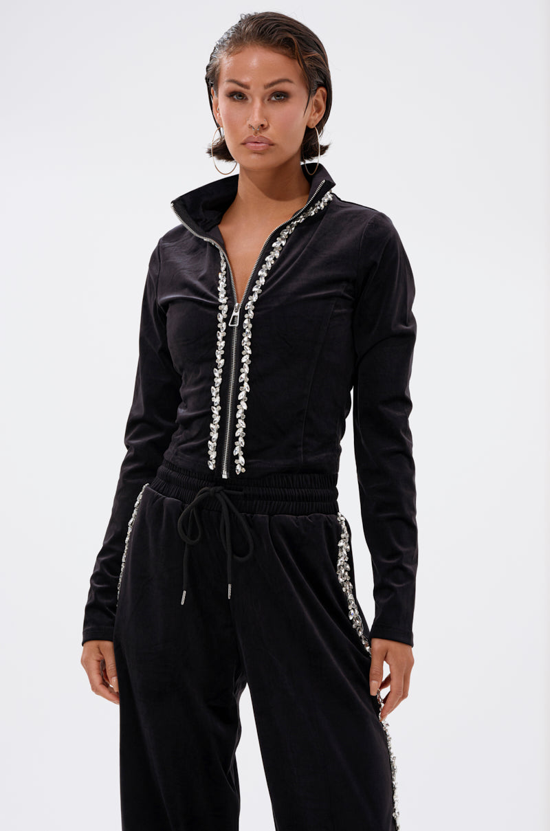 A woman stands against a plain white background wearing the DARA RHINESTONE MOCK NECK ZIP-UP SWEATSHIRT and matching black drawstring pants.