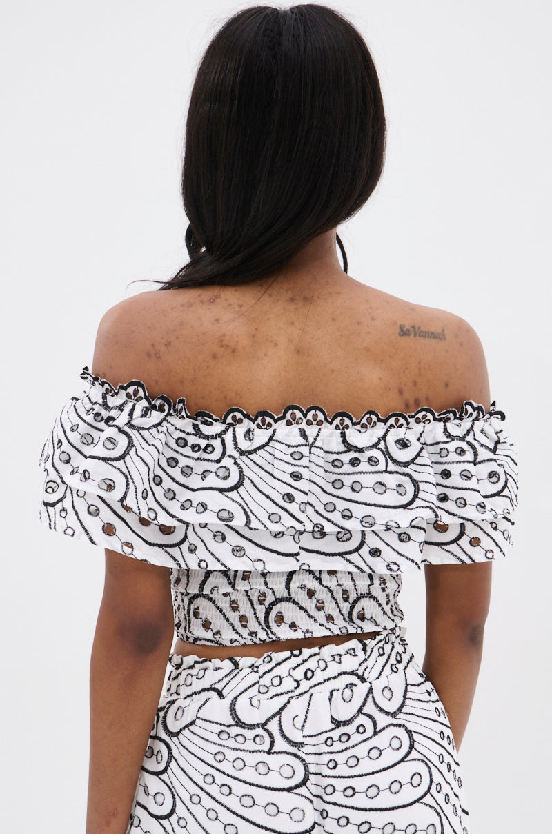 A woman with long dark hair stands with her back to the camera, wearing the SET YOU FREE OFF THE SHOULDER BLOUSE and matching skirt in an abstract stitched pattern. A tattoo appears on her upper right back.