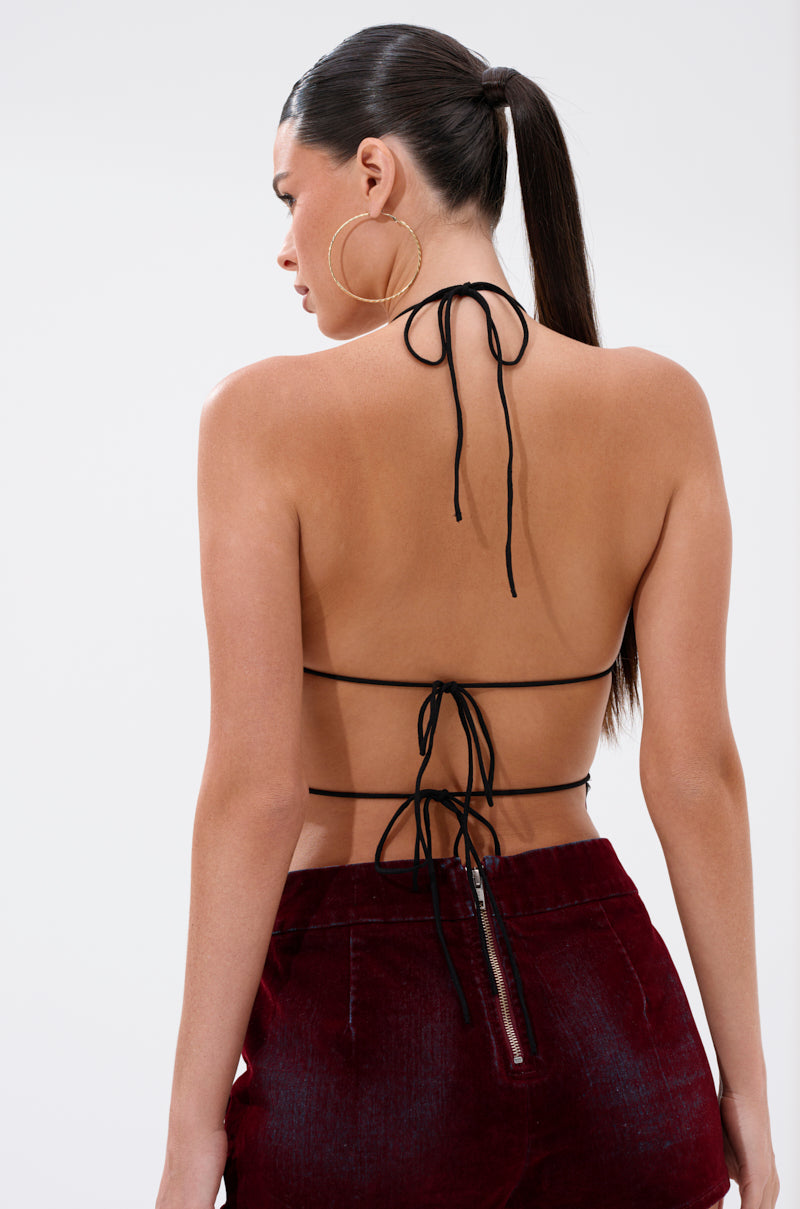 A woman with dark hair in a sleek ponytail wears the BUTTERFLY EFFECT IN OXBLOOD: a strappy backless butterfly halter top and high-waisted cropped burgundy velvet pants, styled with large hoop earrings, shown from the back on a white background.