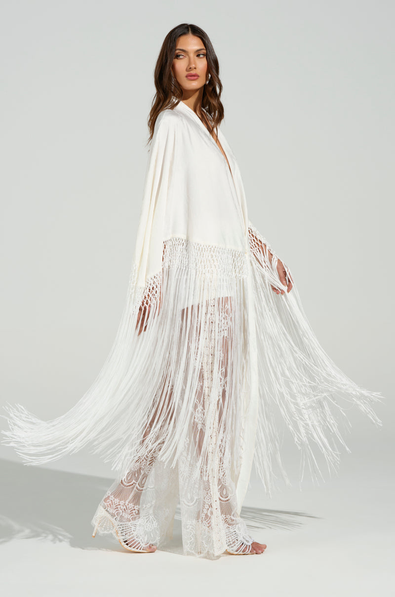 A woman wearing the "On to Something Good Fringe Tie Front Blouse" with a tonal fringe trim and lace patterns poses against a light background, highlighting its elegant design and subtle floral accents.