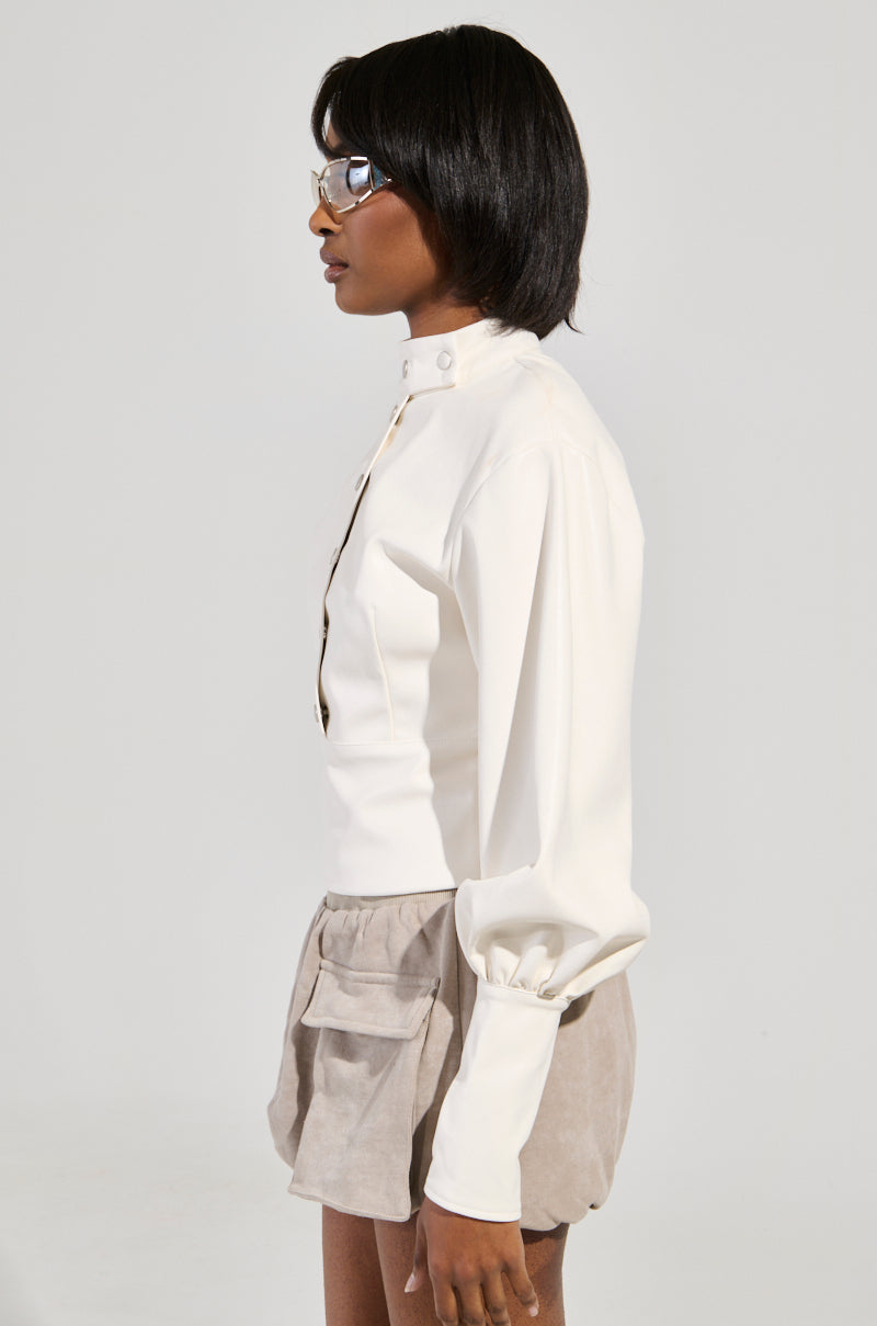 Wearing the "Not Your Normal Biker Chick Top," a person with shoulder-length hair and glasses stands in profile view against a light gray background, paired with beige shorts featuring pockets.