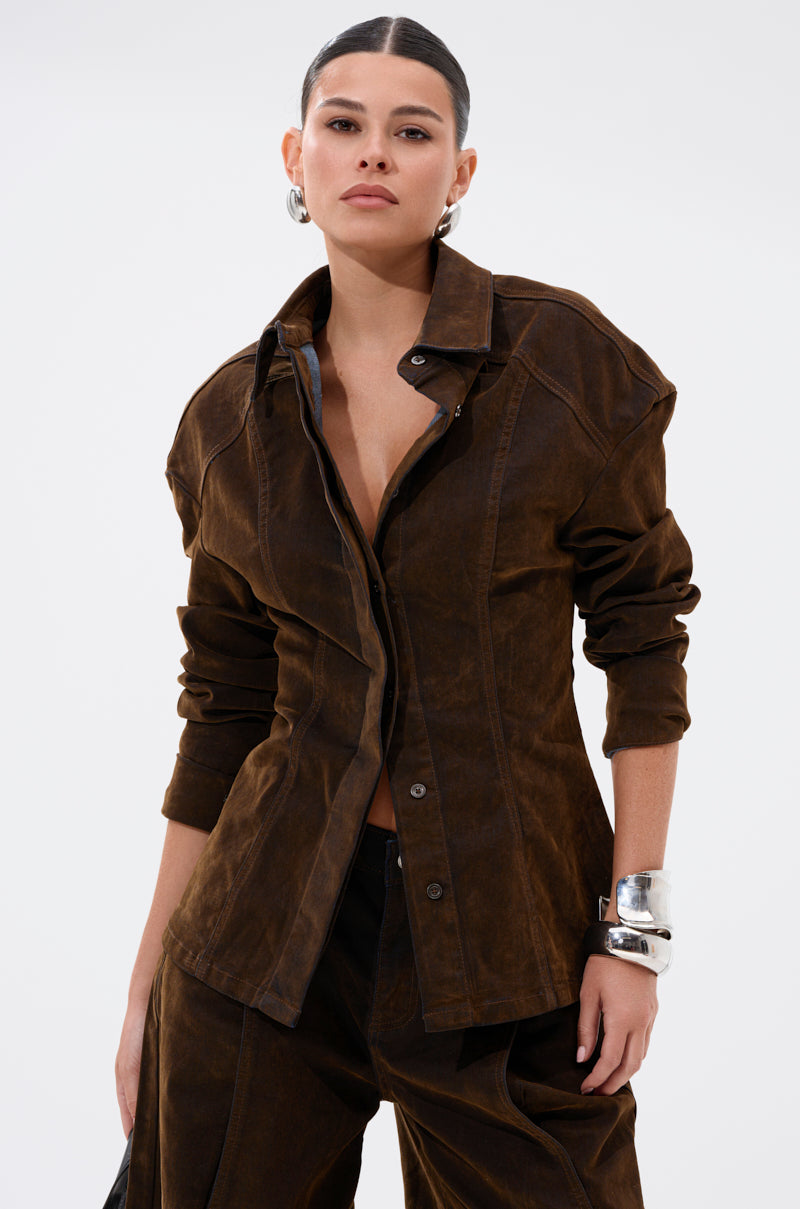 A woman with dark hair pulled back models the FALL VIBES VELVET DENIM BUTTON DOWN with matching pants, styled for fall. She accessorizes with silver hoop earrings and a chunky bracelet, posing confidently against a light background.