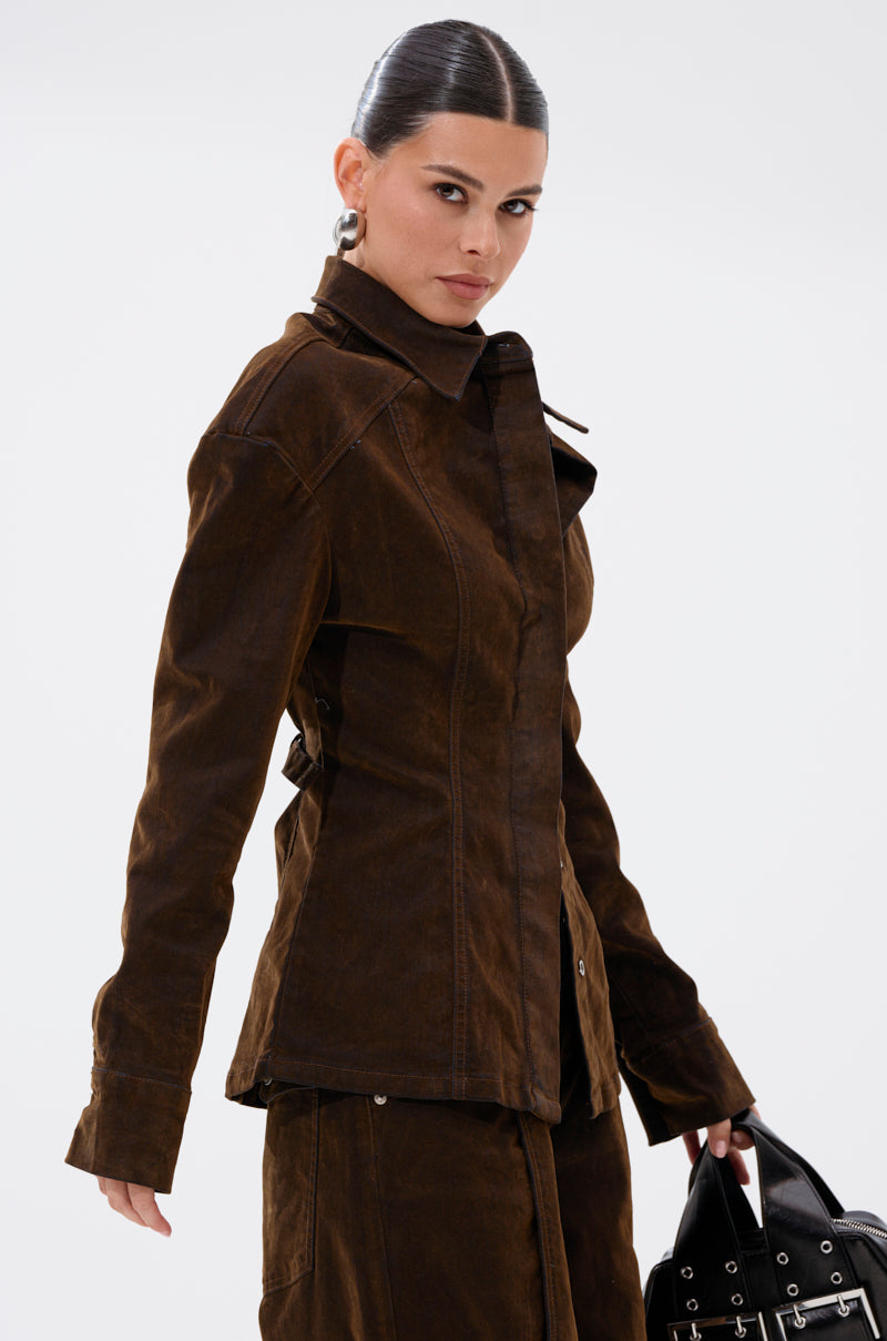 A woman with slicked-back hair wears the FALL VIBES VELVET DENIM BUTTON DOWN and a matching skirt, holding a black handbag. She looks confidently at the camera against a plain light background, showcasing refined fall fashion.