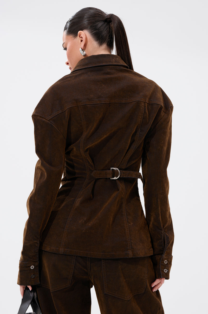 A woman with dark hair in a ponytail models the FALL VIBES VELVET DENIM BUTTON DOWN and matching pants, seen from behind against a white background. She holds a small black bag in her left hand.