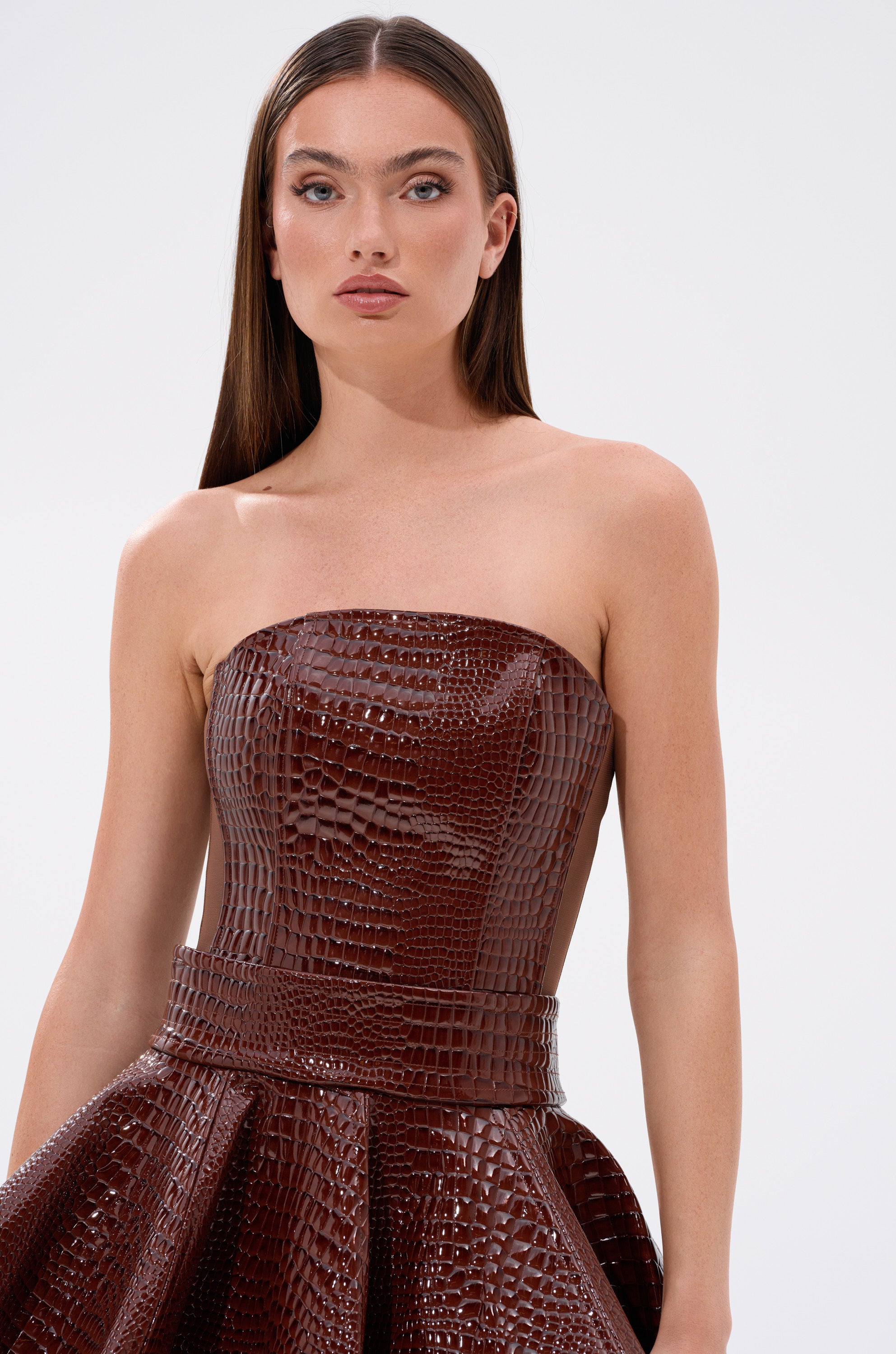 A woman in the TOO GOOD FOR YOU CROCODILE CORSET, a brown dress with a sleek patent faux leather finish.