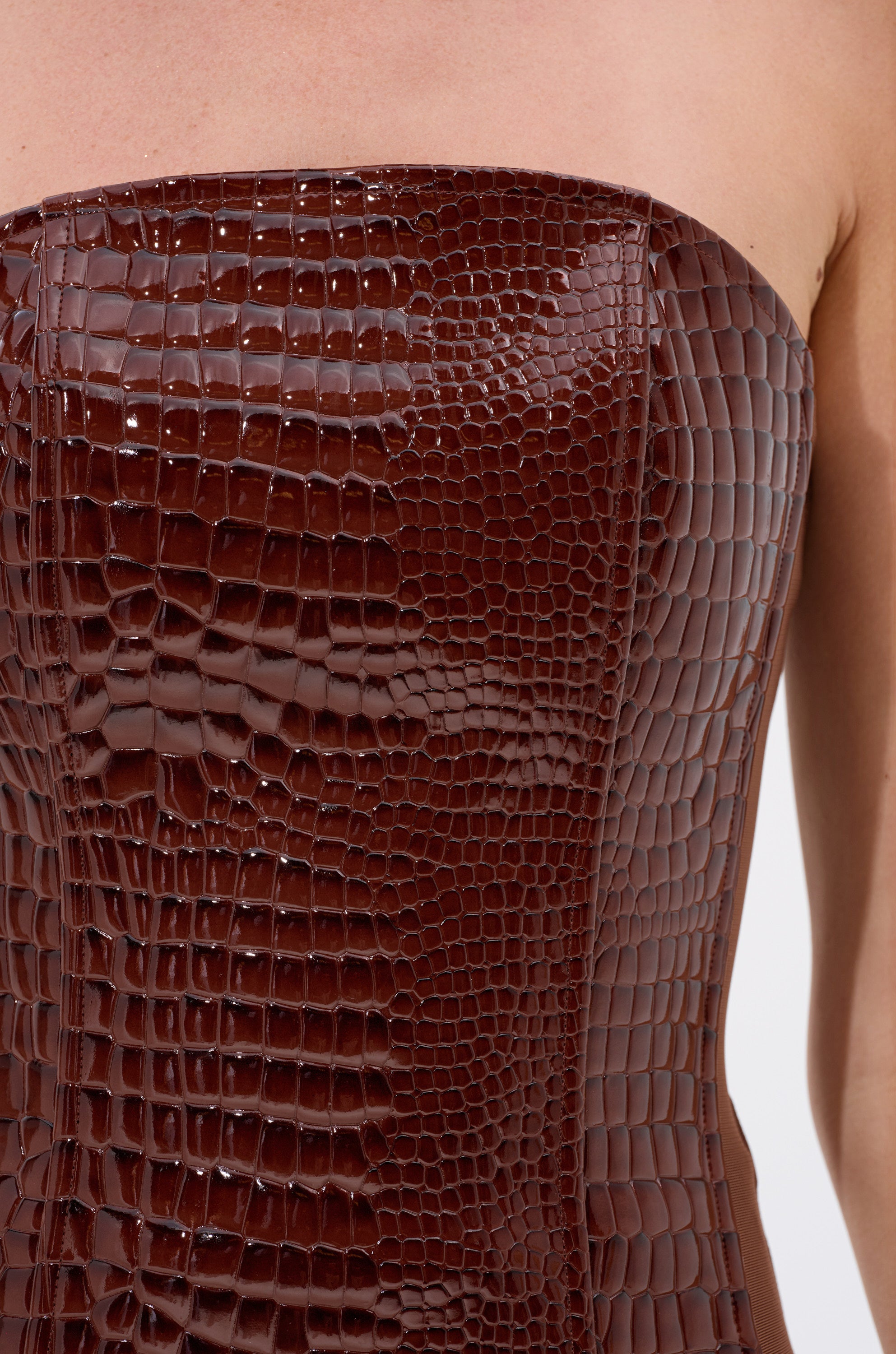 Close-up of the TOO GOOD FOR YOU CROCODILE CORSET, a strapless brown faux crocodile leather piece worn by a person, showcasing its shiny, textured reptile pattern and highlighting the upper chest and shoulders.