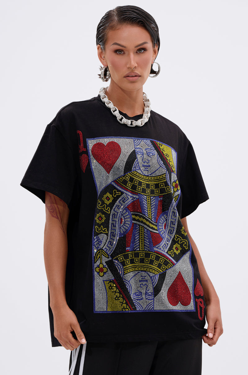 A woman with wet-look hair and hoop earrings wears THE REAL QUEEN OF HEARTS OVERSIZED TEE, a black tee featuring a bold, colorful Queen of Hearts playing card graphic, styled with a chunky silver chain necklace.