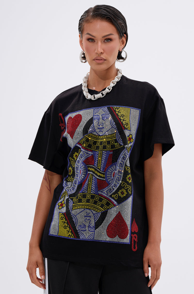 A woman with wet-look hair and silver hoops wears a chunky chain and THE REAL QUEEN OF HEARTS OVERSIZED TEE, featuring a beaded playing card graphic. She stands against a plain light background.