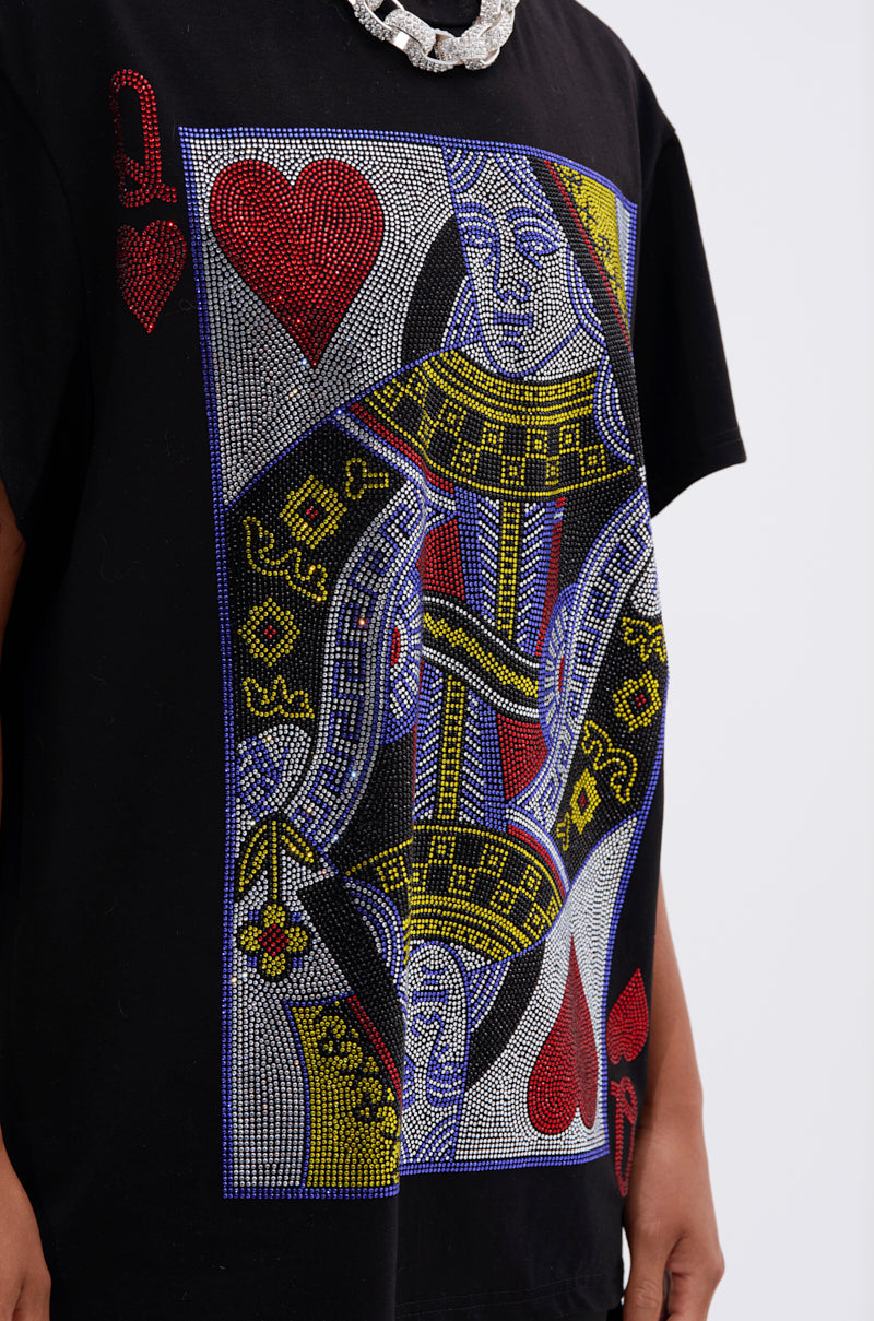 Wearing THE REAL QUEEN OF HEARTS OVERSIZED TEE featuring a bold, rhinestone-adorned playing card graphic, the person (face not shown) styles the statement shirt with a chunky silver necklace.