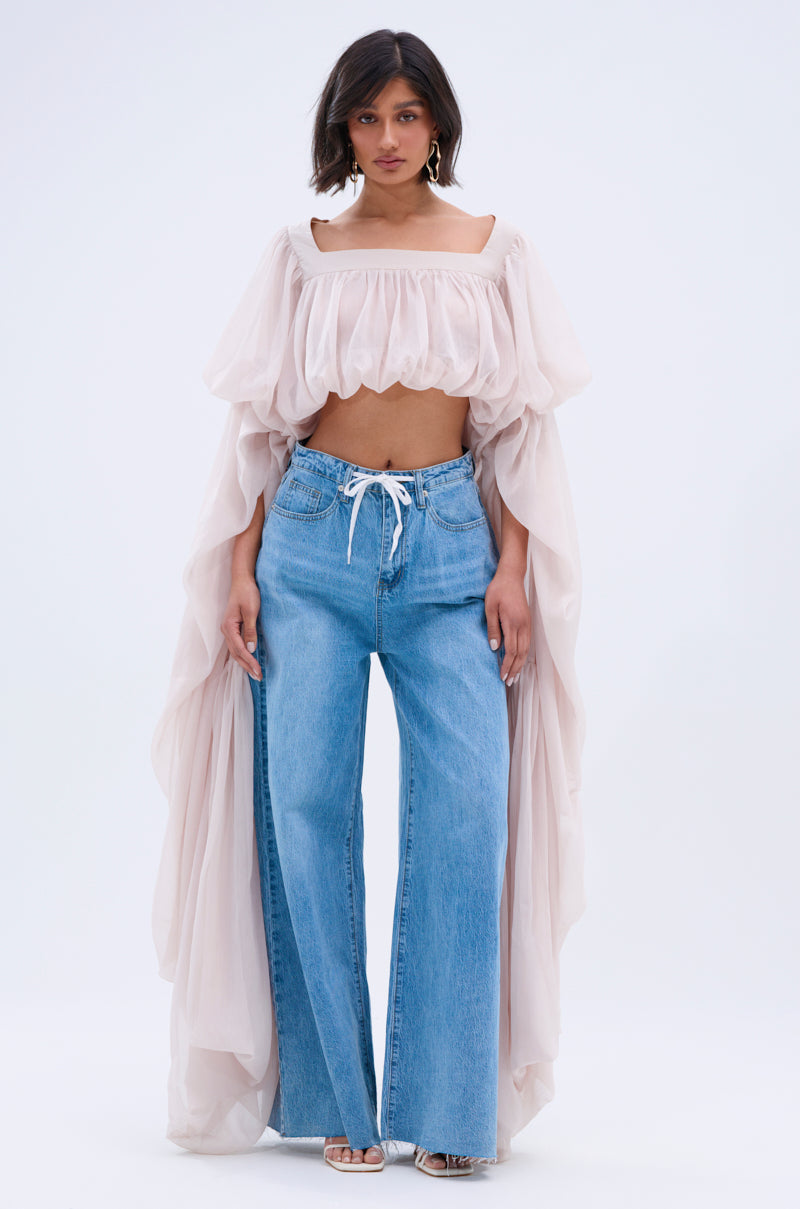 A person stands facing forward, wearing loose blue jeans with a white drawstring and a SLOUCHY SQUARE NECK LONG SLEEVE BLOUSE TOP featuring billowy sleeves and sheer fabric draping at the sides.
