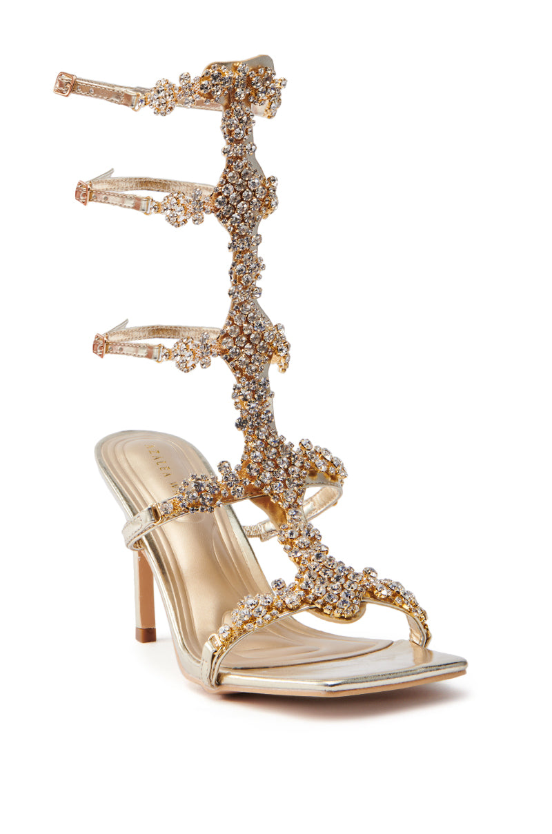 The AZALEA WANG JONQUIL GOLD EMBELLISHED GLADIATOR SANDAL is crafted from metallic faux leather, featuring sparkling rhinestones and an elegant tall strap that wraps up the ankle, secured with multiple stylish buckles.