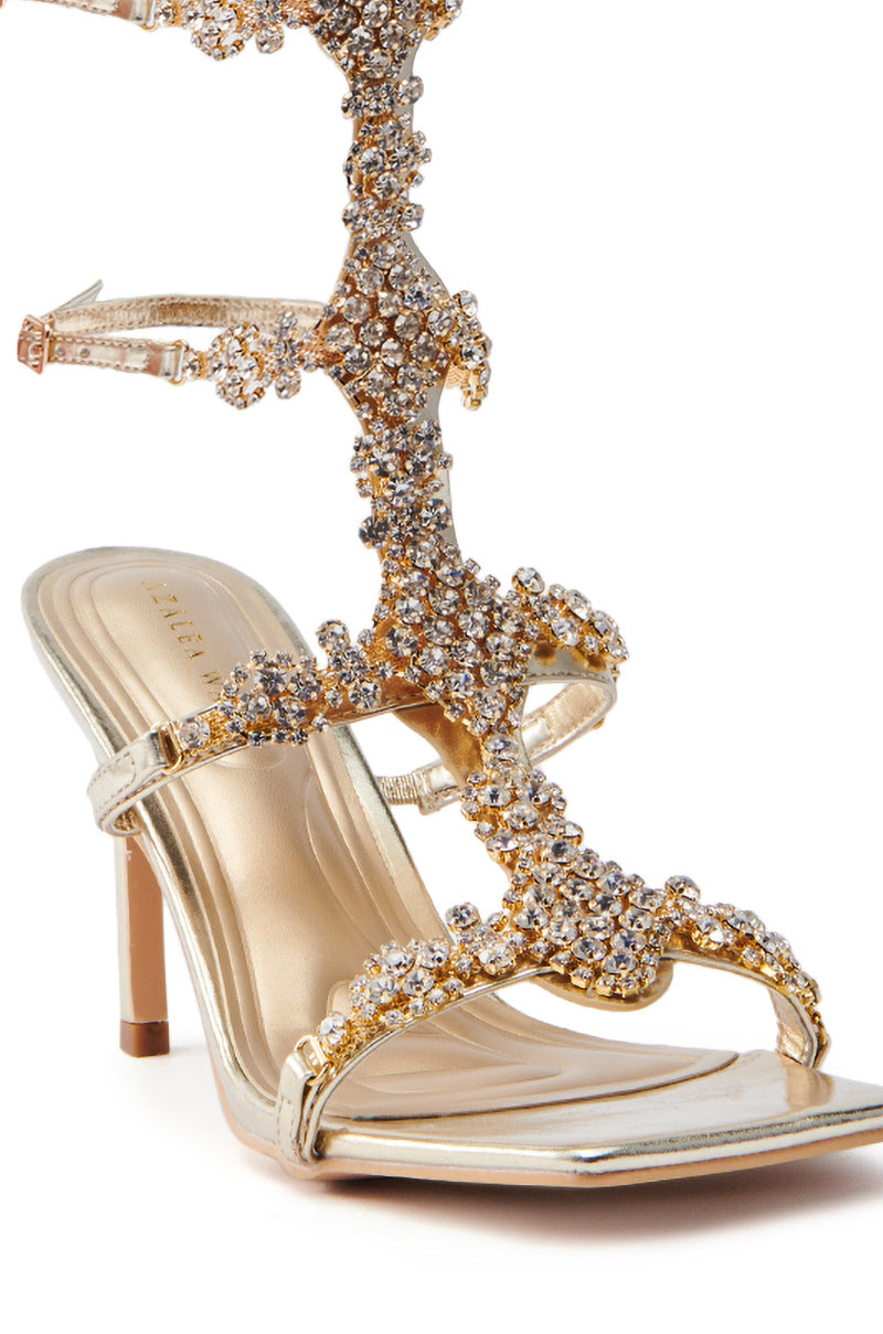 The AZALEA WANG JONQUIL GOLD EMBELLISHED GLADIATOR SANDAL is an exquisite gladiator sandal showcasing sparkling rhinestone embellishments on intricate metallic faux leather straps with a gold finish, all set against a white background.