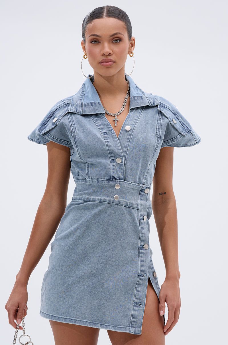 A woman models the NEVER TOO MUCH DENIM MINI DRESS—a short-sleeve, collared mini with a side slit—styled with layered necklaces and hoops against a light backdrop, making it your perfect day-to-night look.