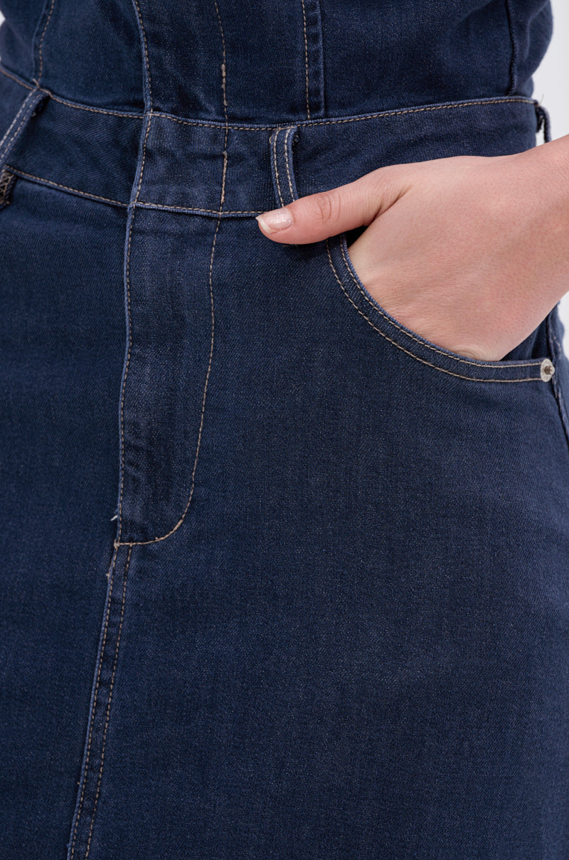 Close-up of a person wearing the LUNA DENIM MAXI DRESS with one hand in the front pocket, highlighting the dress's dark-wash denim, detailed stitching, and textured fabric.
