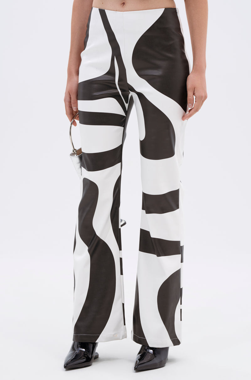 A person wears the GROOVE ON FAUX LEATHER FLARE TROUSER featuring a bold black-and-white abstract swirl print, paired with pointed black shoes. The image is cropped waist to feet against a plain white background.