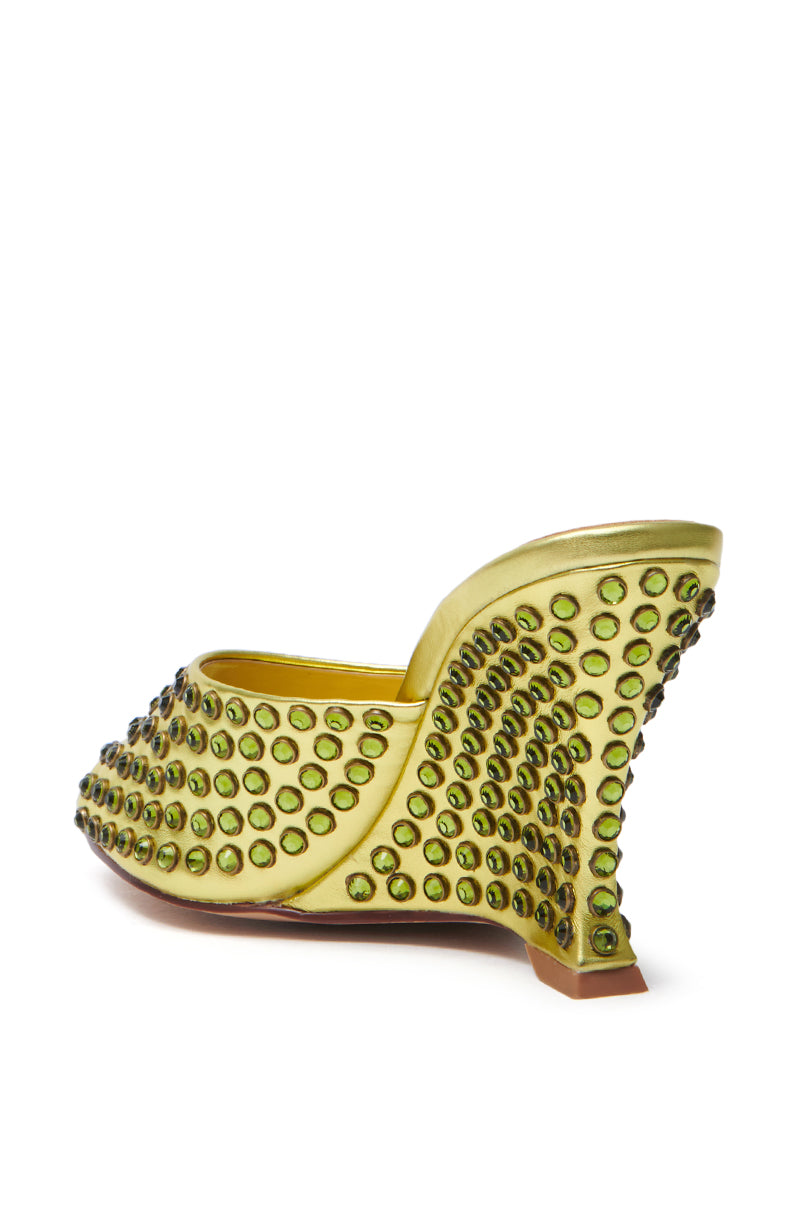 The AZALEA WANG Junius sandal is a green wedge with a unique curved heel, crafted from faux leather and adorned with numerous round gemstones. It features an open back design and an almond-shaped toe, making it a standout piece for any collection.