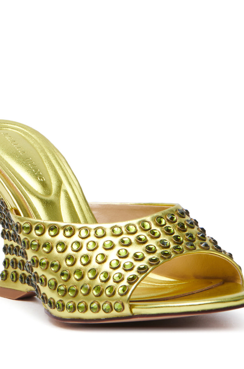 A close-up of the AZALEA WANG JUNIUS GOLD EMBELLISHED WEDGE SANDAL features a glossy, metallic gold finish with rhinestone embellishments, Comfort Cushion Insole, open toe, and medium-height heel adorned with matching studs for elegance.