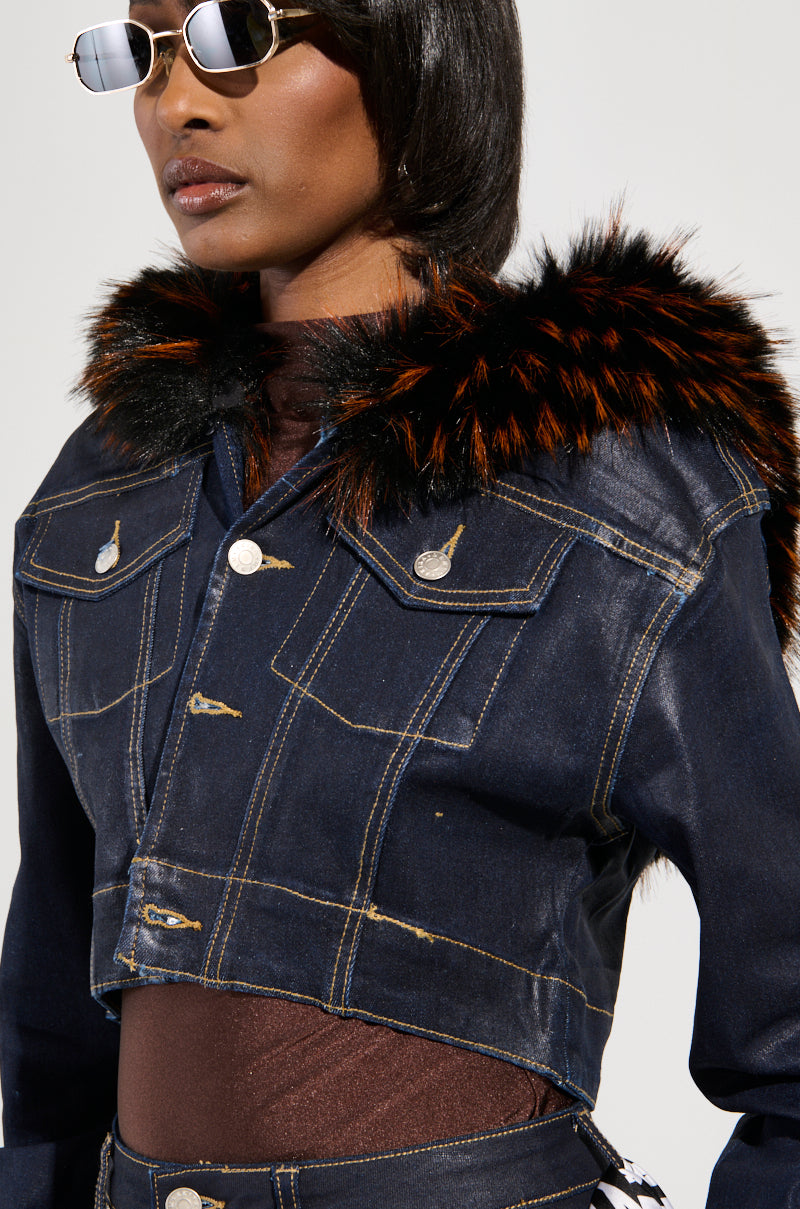 A model wearing sunglasses showcases the SITTING PRETTY FUR TRIM COATED DENIM JACKET, which features a Y2K-inspired dark denim design with eye-catching orange and black faux fur trim on the shoulders. The jacket's prominent stitching and button details are highlighted against a plain background to emphasize the ensemble.