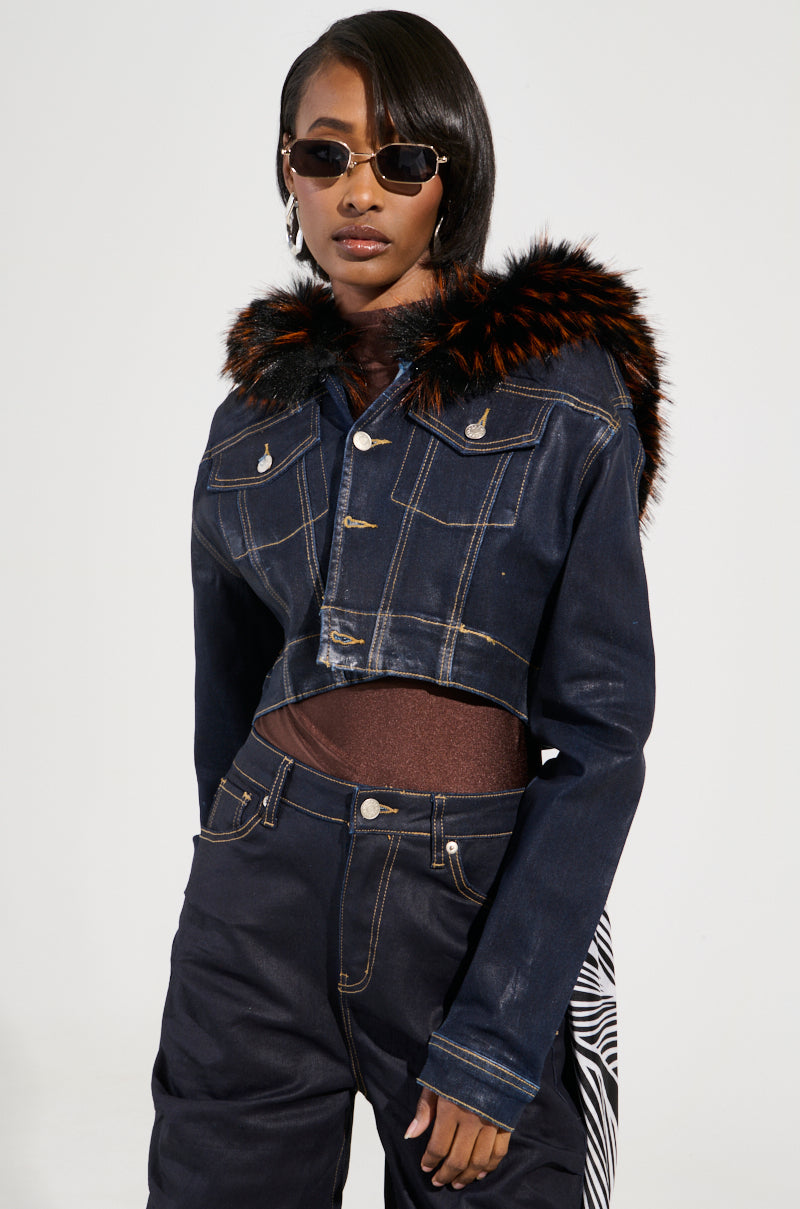 Wearing the SITTING PRETTY FUR TRIM COATED DENIM JACKET, a person exudes Y2K-inspired style as they pose confidently against a plain background. Their outfit also includes matching denim pants and a brown top, accessorized with stylish sunglasses.