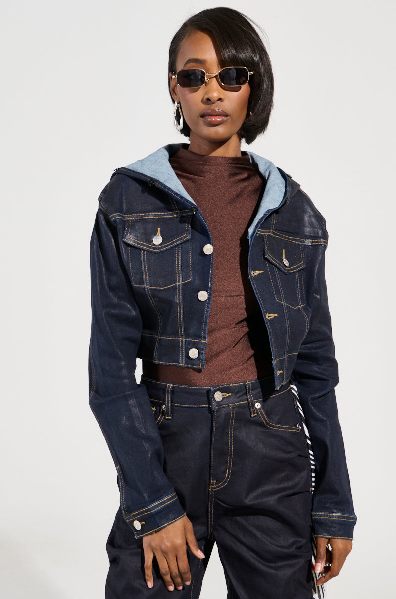A person wearing the SITTING PRETTY FUR TRIM COATED DENIM JACKET, featuring a light blue hood, stands against a plain background over a brown top. Embracing Y2K-inspired vibes, they sport sunglasses and medium-length hair, with hands resting in front of their waist.