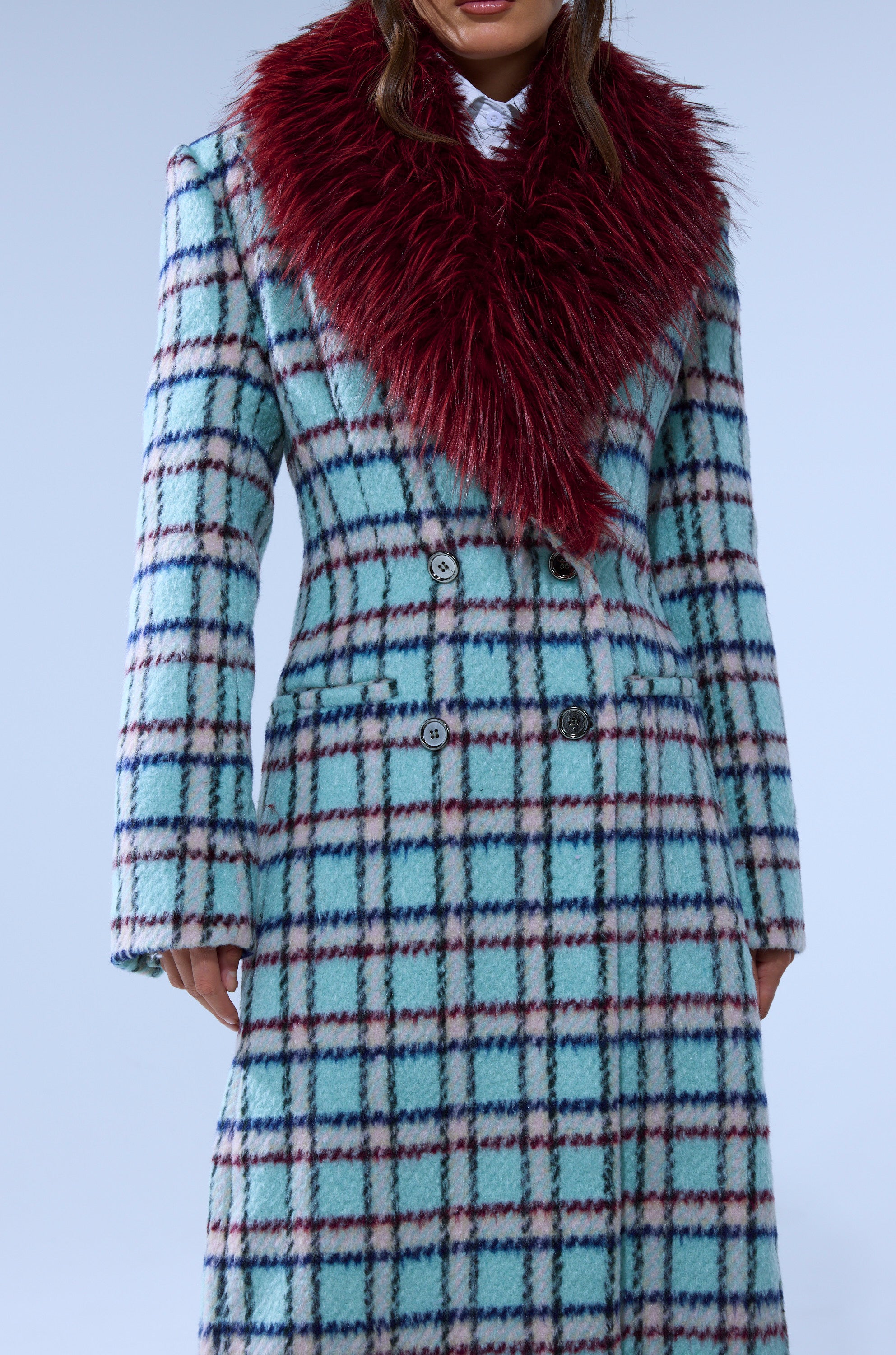 A person models the TEA FOR TWO FUR TRIM TRENCH IN BLUE, a long blue and white plaid coat with a bold deep red faux fur collar, shown from shoulders to knees against a plain light background.