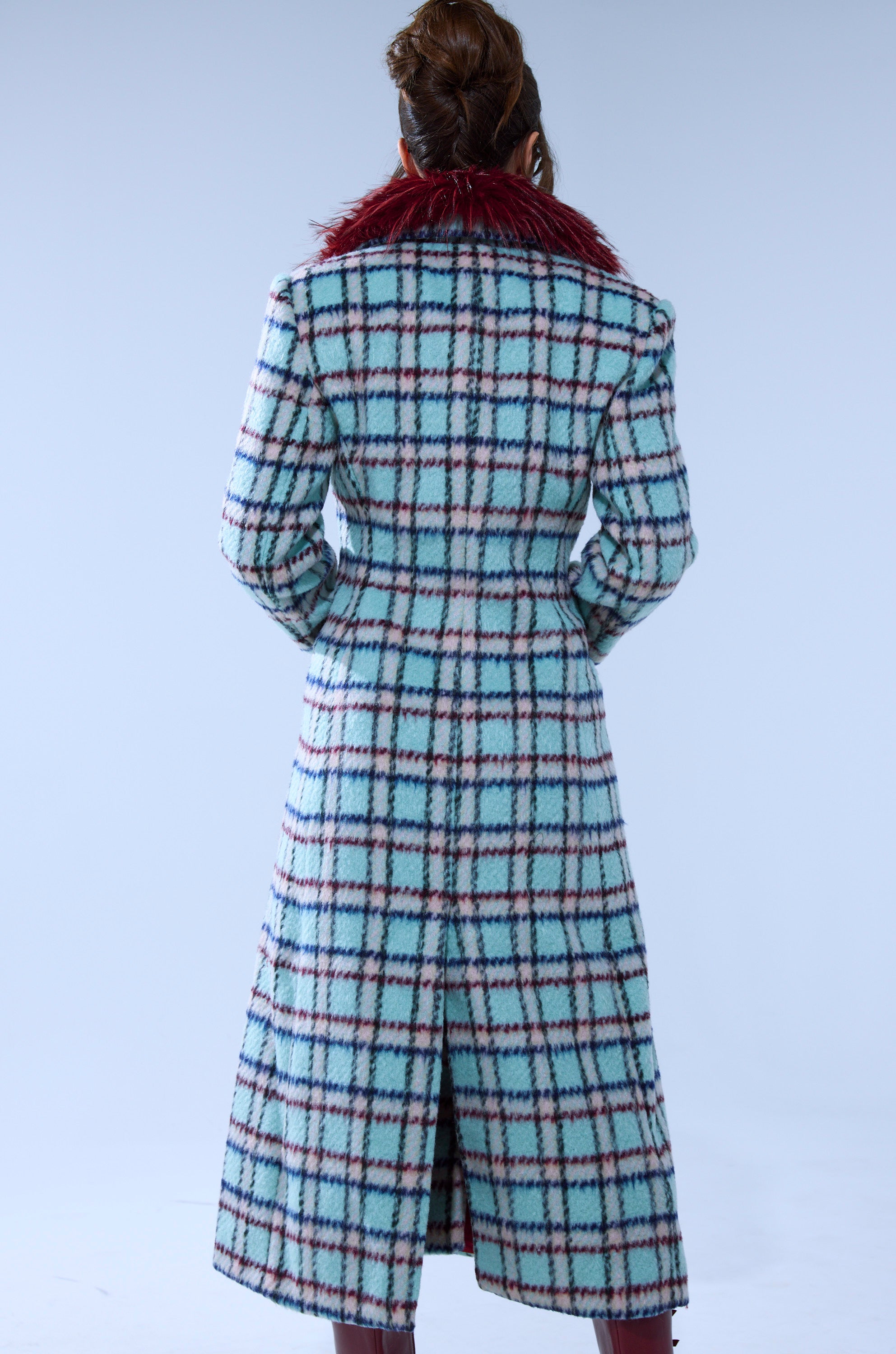 A person with brown hair in an updo is wearing the TEA FOR TWO FUR TRIM TRENCH IN BLUE, featuring blue plaid and a red faux fur collar, standing with their back to the camera against a plain light background.