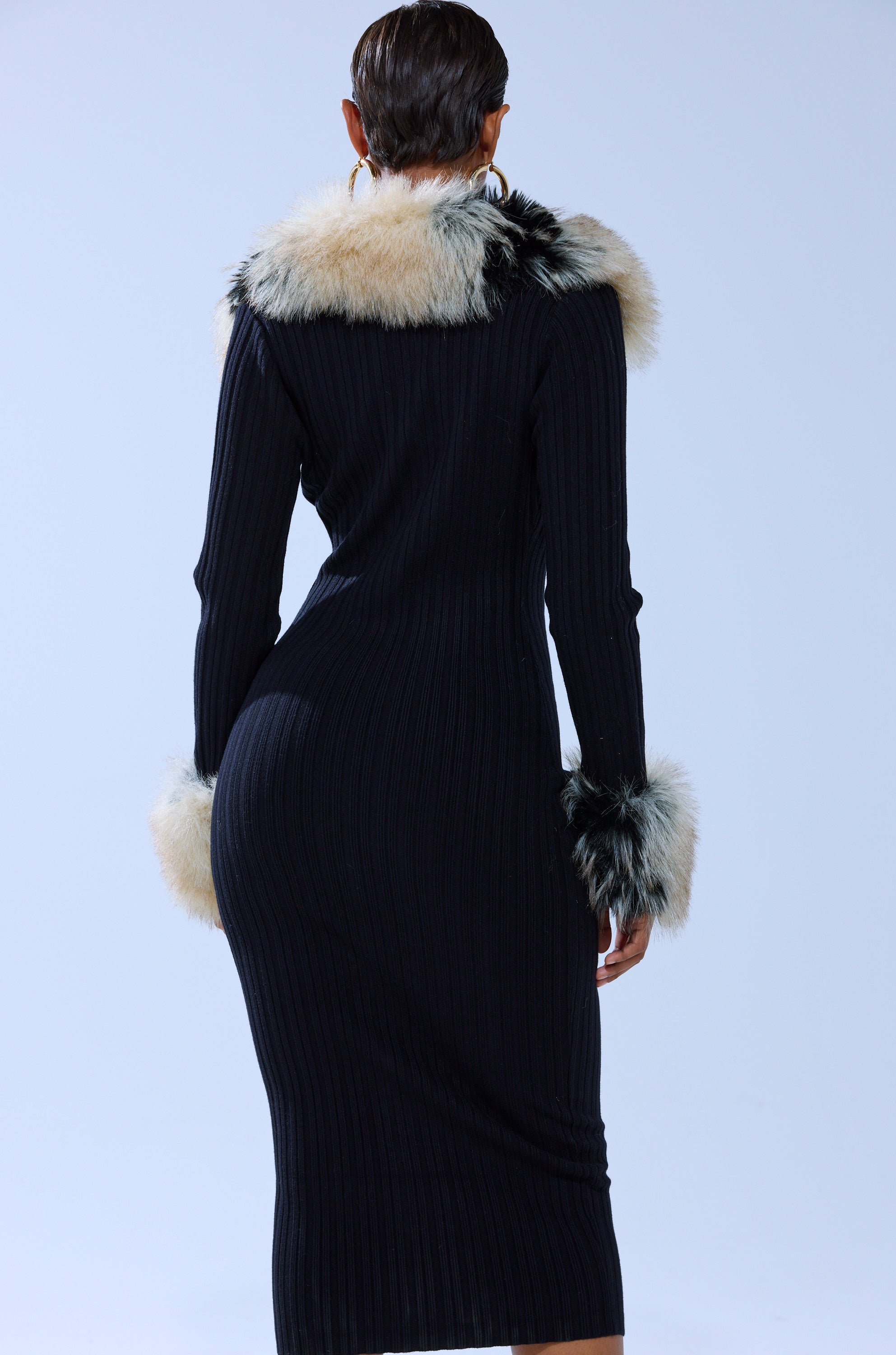 A person with short hair, seen from behind against a light blue background, wears the MICHELLE KNIT MIDI DRESS WITH FUR ACCENTS—featuring ribbed knit fabric and light-colored faux fur on the collar and cuffs.