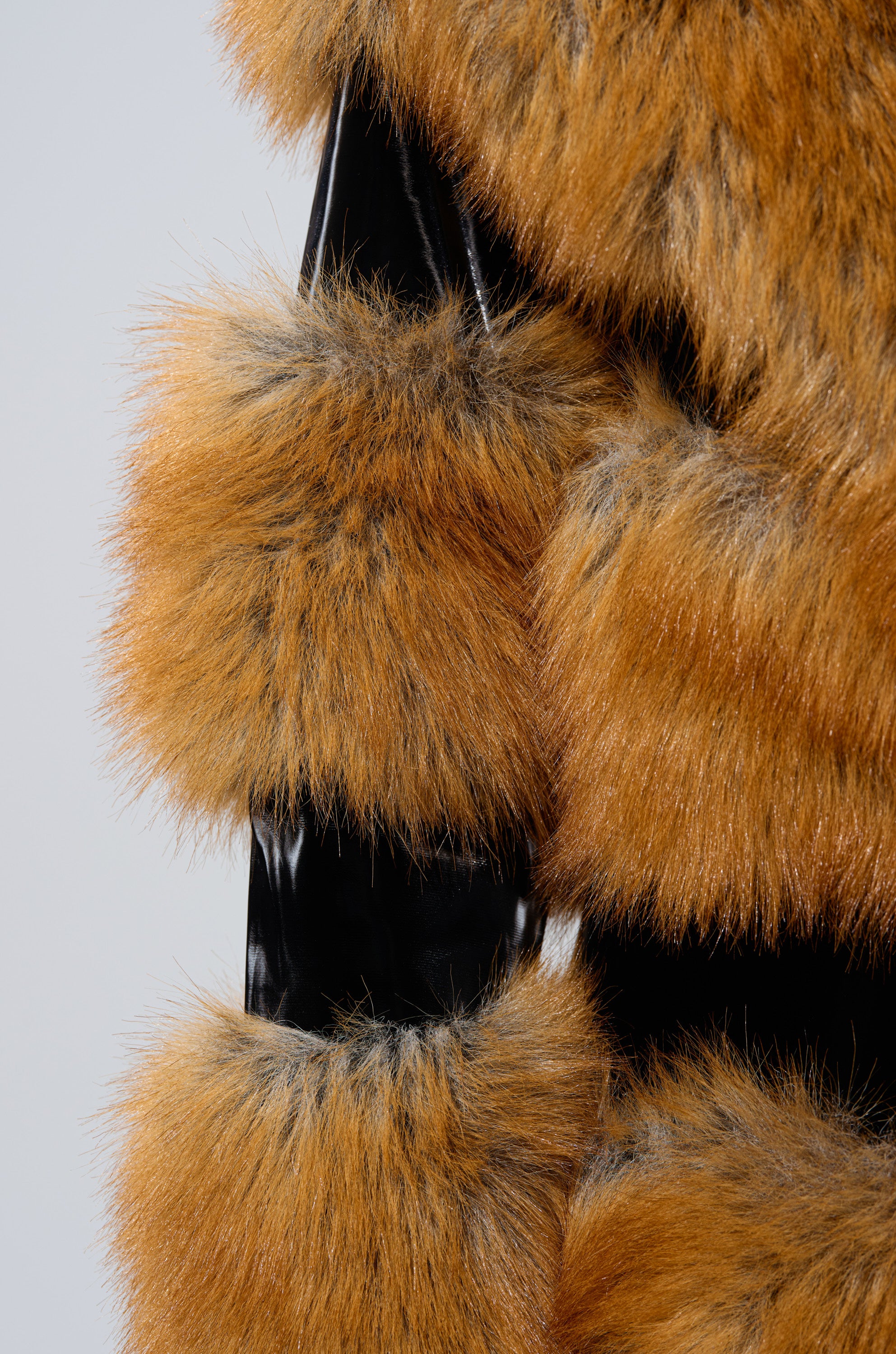 A close-up of the MADDOX PANELED FAUX FUR coat, featuring alternating horizontal bands of shiny black material and thick, orange-brown faux fur with dark tips against a plain light gray background.