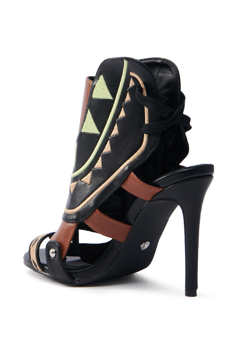 The AZALEA WANG MERAKI BLACK AND BONE SANDAL is a high-heeled, color block sandal with a unique design featuring black, brown, and tan straps. It boasts a decorative black cover with light green triangles and tan geometric patterns in vegan leather for a bold, modern look.