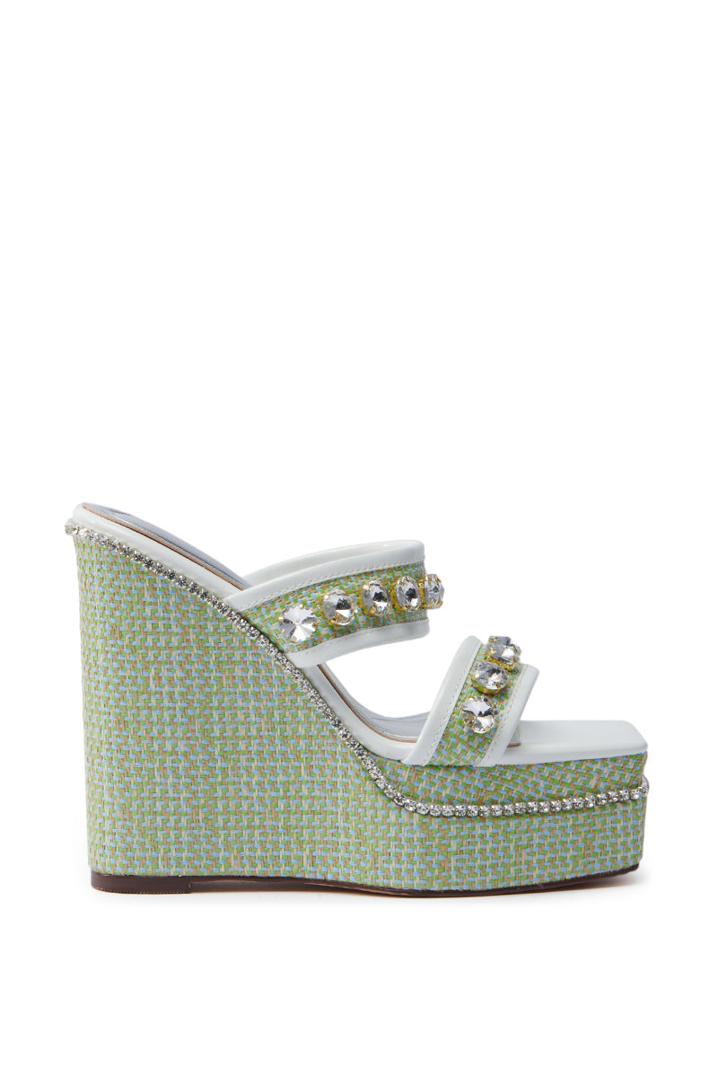 Discover the AZALEA WANG NIOMA Green Embellished Wedge Sandal, a fashionable shoe with a chunky wedge heel and platform sole. It boasts two straps with large round gemstones and a vibrant woven texture in blue and green for an eye-catching style.
