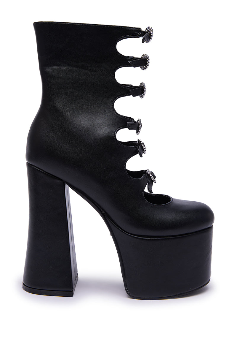 The AZALEA WANG OMLEE BLACK ULTRA HIGH PLATFORM BOOTIE is a black faux leather bootie with a chunky heel, five decorative front buckles, and a round cutout near the toe.