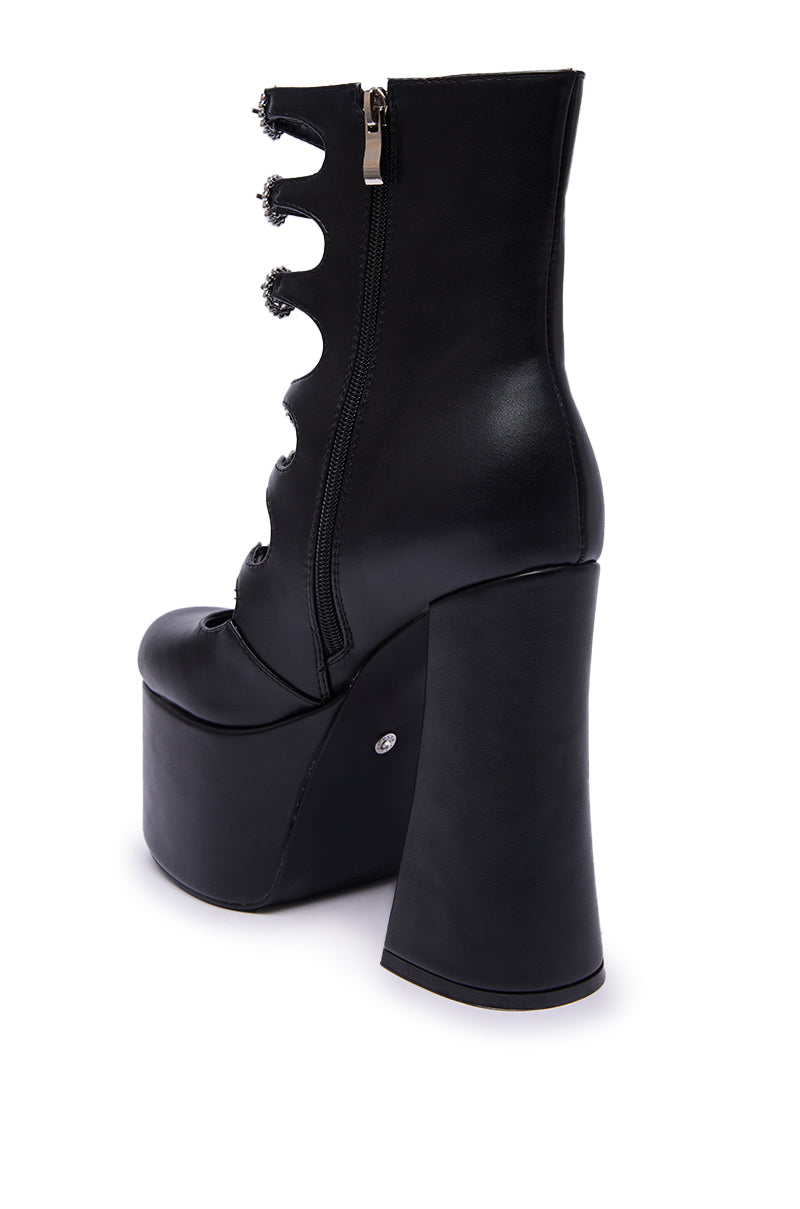 The AZALEA WANG OMLEE BLACK ULTRA HIGH PLATFORM BOOTIE features a black faux leather design with a chunky heel, side zipper, and decorative circular cutouts, showcased against a white background for a modern, edgy look.