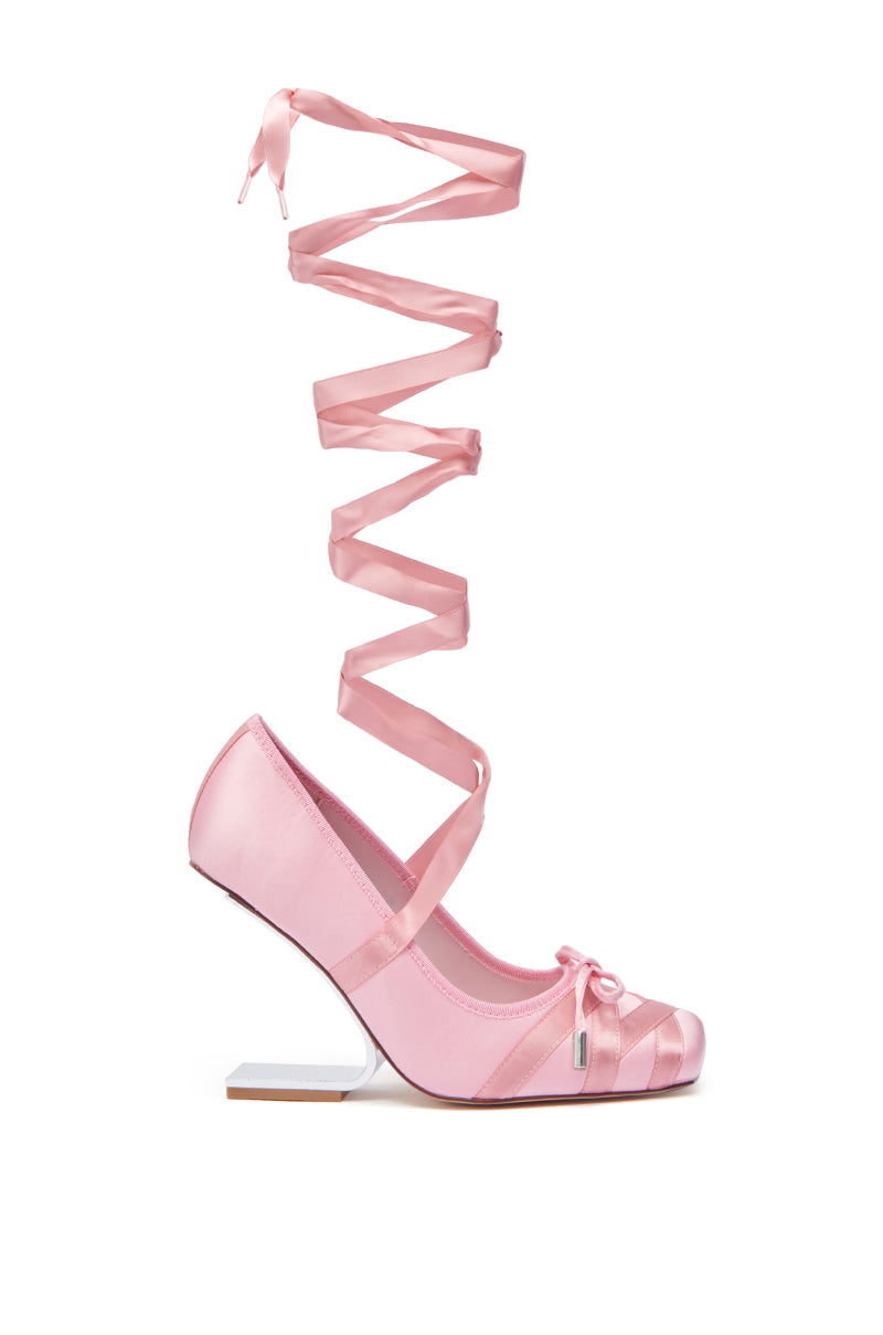 The AZALEA WANG PAVARTI PINK BALLET PUMP features a pink satin upper, square white inverted wedge heel, and long pink satin ribbon laces for a ballet-inspired look.