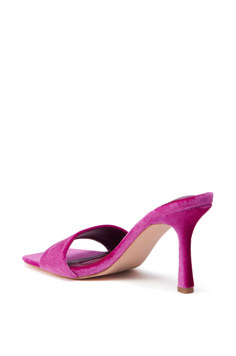 The AZALEA WANG PERSUASION FUCHSIA SANDAL is elegantly showcased on a white background, featuring an open back design with a sleek stiletto heel. It flaunts a soft velvet upper, adorned with crisscrossing straps over the foot.