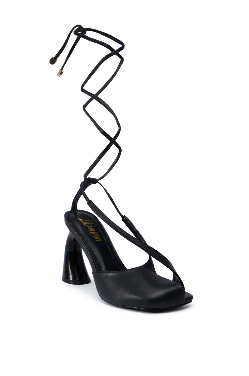 The Pirate Black Pump features a black strappy design with an open toe and thin straps that intricately crisscross around the ankle. The moderately high, tapered heel adds an elegant and sophisticated touch.