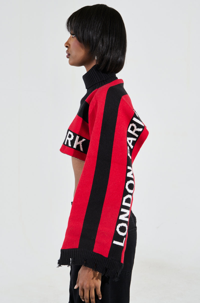 A person with short hair models the New York Ultra Crop Sweater in Red Multi featuring a striking black and red colorblock pattern. The long sleeves boldly display "LONDON" and "PARK," while a plain white background accentuates its modern design.
