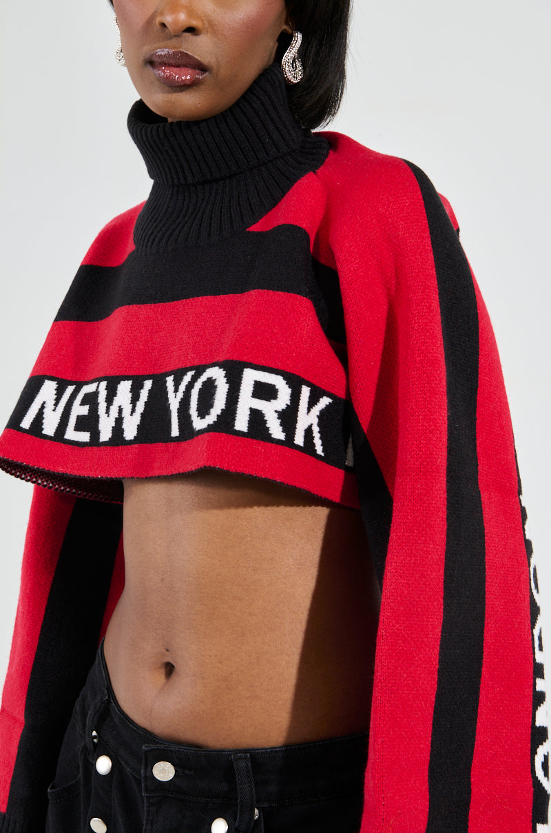 A person is wearing the fashionable New York Ultra Crop Sweater in Red Multi, which pairs perfectly with chic black pants featuring stylish button details.