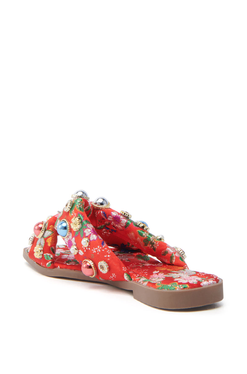 The AKIRA RAMSEY RED FLAT SANDAL flaunts a red, floral-patterned satin design with crisscross fabric straps adorned with colorful beads. Its brown flat sole and soft cushioned insole promise both style and comfort.