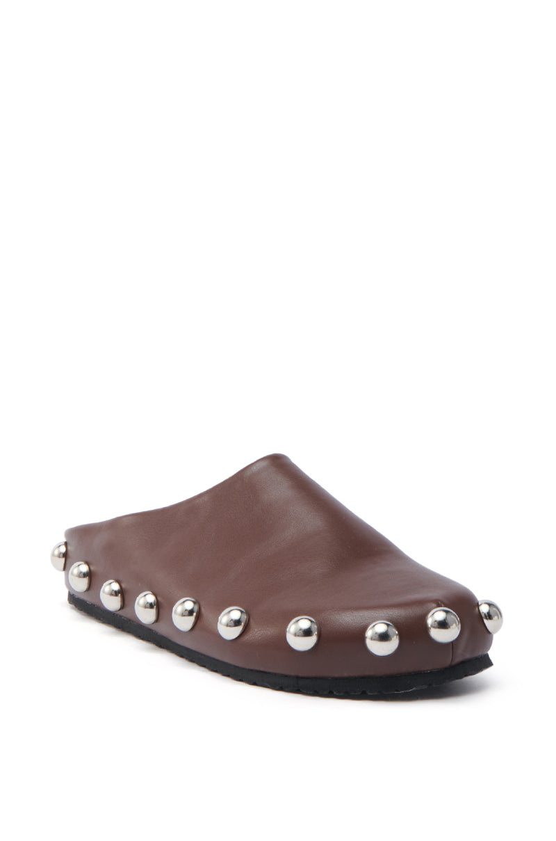 The AZALEA WANG RAYNE BROWN FLAT is a vegan leather slip-on shoe featuring an almond toe and flat black sole, embellished with shiny silver spherical studs around the perimeter. It is shown at a three-quarter angle.