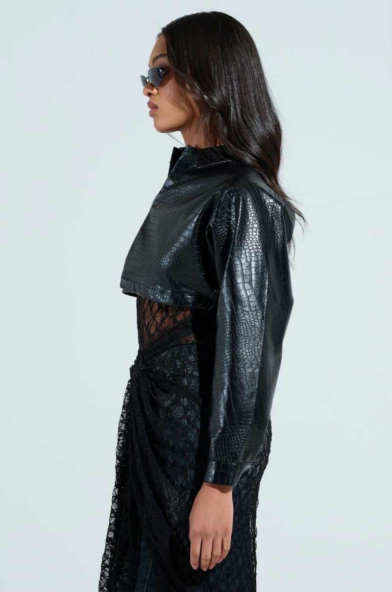 A woman in NATALIA CROCODILE PU BUTTON DOWN SHIRT, sunglasses, and a black lace dress, stands in profile against a light grey background.