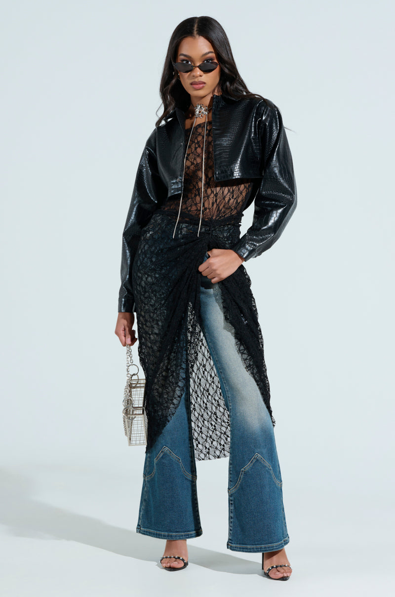 A trendy individual sports sunglasses with a chic, cropped look by wearing the NATALIA CROCODILE PU BUTTON DOWN SHIRT over a sheer lace top, paired with flared jeans and a textured handbag—an impeccable blend of modern textures and patterns.