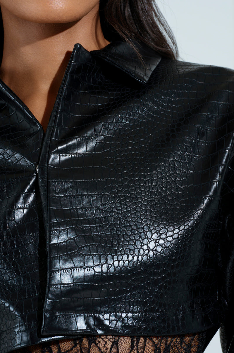 A close-up of a person wearing the NATALIA CROCODILE PU BUTTON DOWN SHIRT in shiny faux crocodile leather with a structured collar and lace details under the cropped silhouette.